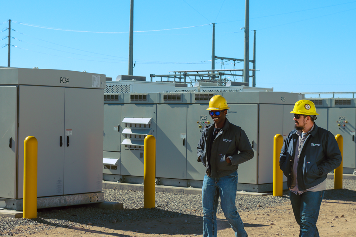 Two Energy Storage Workers with hardhats walking next to energy storage units.