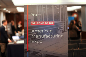 Sign with SEIA, Welcome to the American Manufacturing Expo in a room with people in the background.